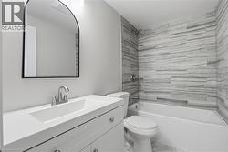 White vanity with integrated sink, brushed nickel faucet, arched mirror, and tiled shower surround with bathtub - 