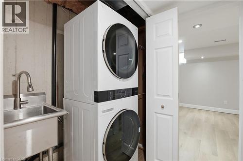 Stacked laundry appliances, stainless steel utility sink with gooseneck faucet, light wood-finish flooring, and recessed ceiling lighting - 30 S Imperial Road Unit# 3, Guelph, ON 