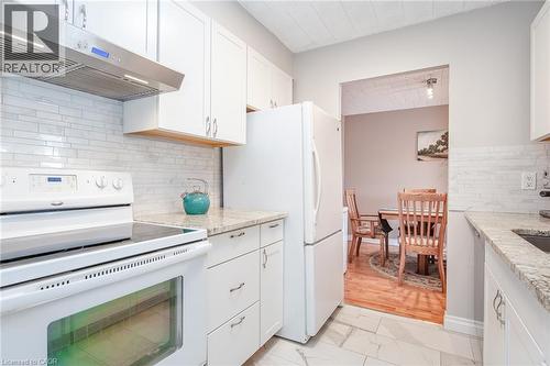 Kitchen featuring white cabinetry, light-colored countertops, white subway tile backsplash, stainless steel range hood, and white appliances - 71 Vanier Drive Unit# 310, Kitchener, ON 