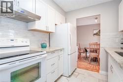 Kitchen featuring white cabinetry, light-colored countertops, white subway tile backsplash, stainless steel range hood, and white appliances - 