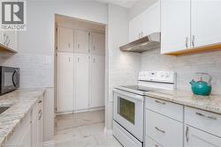 White cabinetry, granite-style countertops, mosaic tile backsplash, stainless steel range hood, and tile flooring - 