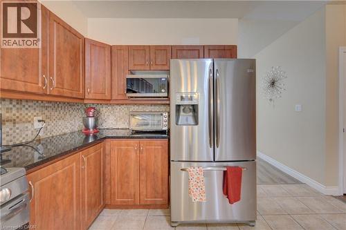 Kitchen featuring cabinetry, dark countertops, a tiled backsplash, and light tile flooring - 78 Stuckey Avenue, Baden, ON 