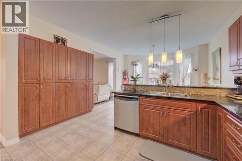 Extensive built-in cabinetry, stainless steel dishwasher, double basin sink, dark countertops, and tile backsplash - 78 Stuckey Avenue, Baden, ON 
