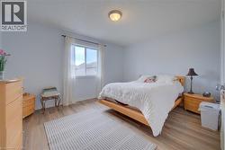 Light wood-finish flooring, single window with white curtains, neutral wall paint, and a ceiling-mounted light fixture - 