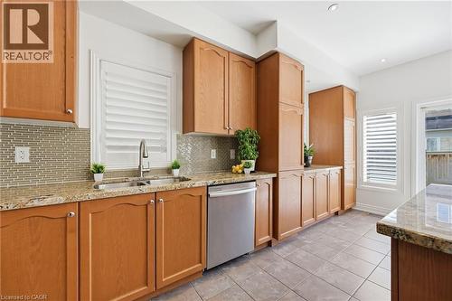 Kitchen featuring extensive wood cabinetry, granite countertops, a tile backsplash, stainless steel appliances, and a double basin sink with a gooseneck faucet - 3198 Tim Dobbie Drive, Burlington, ON 