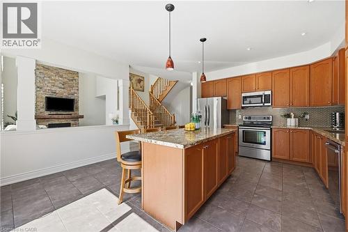 Kitchen featuring a center island with a granite countertop, wood cabinetry, stainless steel appliances, and tile flooring - 3198 Tim Dobbie Drive, Burlington, ON 