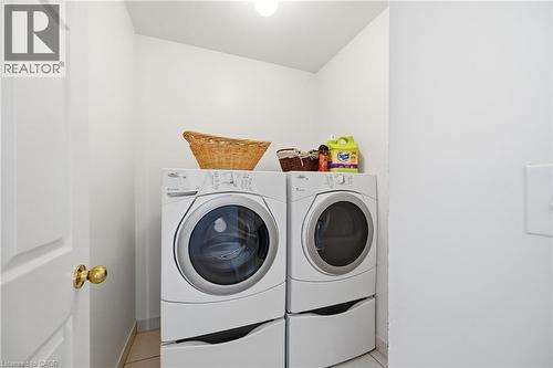 Dedicated laundry area with a white paneled door, brass hardware, and light-toned tile flooring - 3198 Tim Dobbie Drive, Burlington, ON 