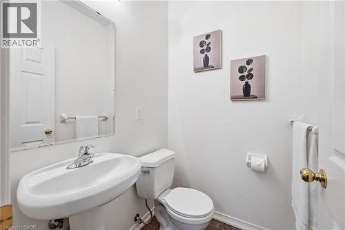 White pedestal sink with a chrome faucet, wall-mounted mirror, and a two-piece toilet - 3198 Tim Dobbie Drive, Burlington, ON 