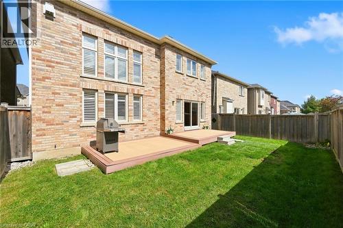 Brick exterior with multiple windows, a ground-level deck, a sliding glass door, and a fenced backyard with a lawn - 3198 Tim Dobbie Drive, Burlington, ON 