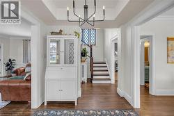 Hardwood flooring, white trim, recessed ceiling with a contemporary chandelier, and a wood staircase with white risers - 