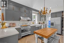 Kitchen featuring grey shaker-style cabinetry, light-toned countertops, herringbone wood-finish flooring, and a stainless steel range with matching hood - 