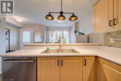 Light wood-finish cabinetry with black hardware, stainless steel sink, integrated dishwasher, and a stone-look tile backsplash - 