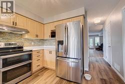 Recessed lighting illuminates the kitchen featuring wood-finish cabinetry, stainless steel appliances, and a tiled backsplash - 