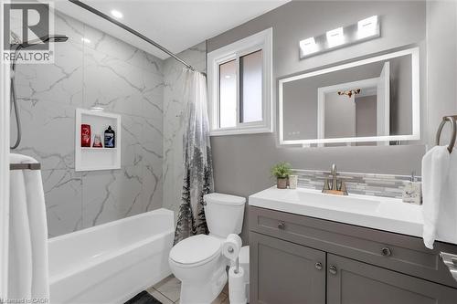 This bathroom features a white bathtub with marble-style tiled walls and a recessed shelf, alongside a toilet - 7506 Jubilee Drive, Niagara Falls, ON 