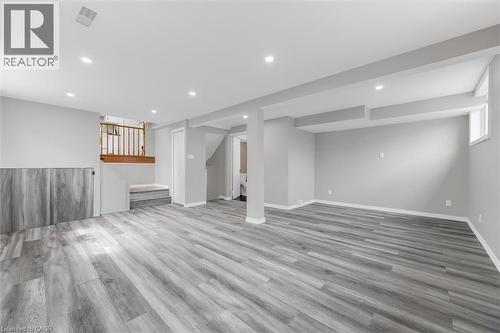 Spacious room featuring light grey walls, grey wood-style flooring, recessed lighting, and a white-framed window - 7506 Jubilee Drive, Niagara Falls, ON 