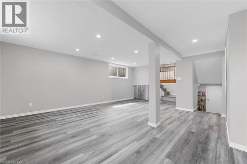 Spacious room featuring light grey walls, grey wood-style flooring, recessed lighting, and a visible window - 7506 Jubilee Drive, Niagara Falls, ON 
