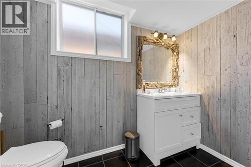 Bathroom featuring wood paneling, black floor tiles, a white vanity with a single sink, and a decorative mirror - 7506 Jubilee Drive, Niagara Falls, ON 