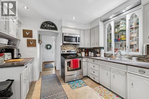 White cabinetry with decorative glass panels, stainless steel appliances, and a tiled backsplash - 80 Maclennan Avenue, Hamilton, ON 