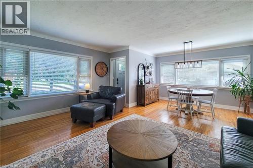 Hardwood flooring throughout, multiple windows with blinds, crown molding, a built-in buffet, and a contemporary linear chandelier - 19 Thorndale Avenue, St. Catharines, ON 