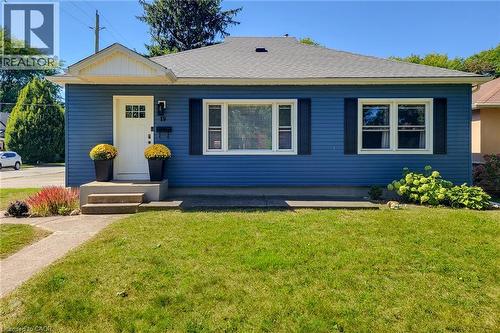 Blue horizontal siding exterior with a contrasting white front door, a gabled entry overhang, and white-framed windows with dark shutters - 19 Thorndale Avenue, St. Catharines, ON 