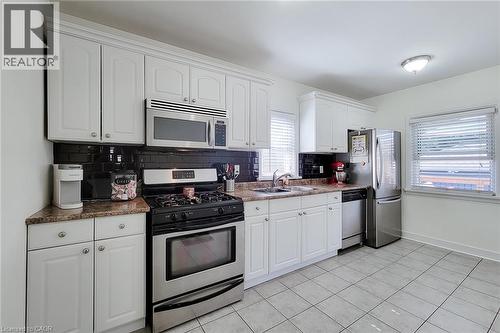 White cabinetry, stainless steel appliances, dark subway tile backsplash, granite-style countertops, and tile flooring - 19 Thorndale Avenue, St. Catharines, ON 