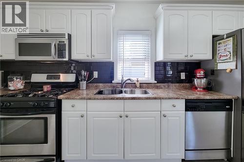 White cabinetry, dark subway tile backsplash, stainless steel appliances, double basin sink, and wood-finish countertops - 19 Thorndale Avenue, St. Catharines, ON 