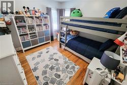 Wood-finish flooring with white baseboards, a built-in bunk bed, and a wall-mounted shelving unit - 