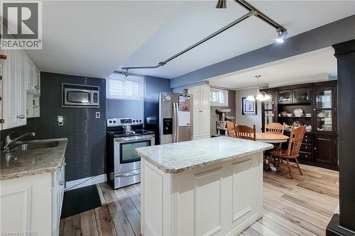 Kitchen featuring a center island with a light-toned countertop, stainless steel appliances, wood-finish flooring, white cabinetry, and a dark tile backsplash - 19 Thorndale Avenue, St. Catharines, ON 