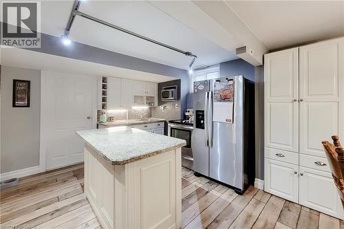 Kitchen featuring wood-finish flooring, an island with a light-toned countertop, white cabinetry with silver hardware, a stainless steel refrigerator, and track lighting - 19 Thorndale Avenue, St. Catharines, ON 