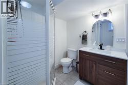 Frosted glass shower enclosure, wood-finish vanity with drawer storage, white countertop with integrated sink, black wall-mounted faucet, and arched mirror - 