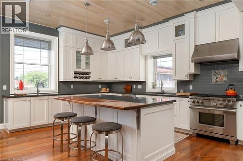 White shaker cabinetry with dark countertops, stainless steel appliances, wood-finish flooring, a wood-paneled ceiling, and a built-in wine rack - 23 Market Street W, Port Dover, ON 