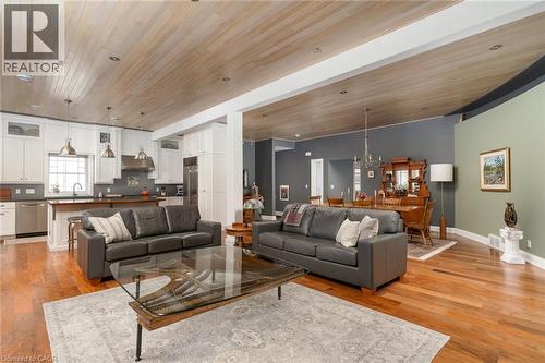 Open-concept living area with hardwood flooring, a wood-paneled ceiling, recessed lighting, and a kitchen featuring white cabinetry and stainless steel appliances - 23 Market Street W, Port Dover, ON 