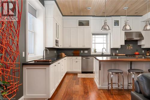 White cabinetry, dark countertops, stainless steel appliances, wood-finish flooring, and a wood-panelled ceiling - 23 Market Street W, Port Dover, ON 