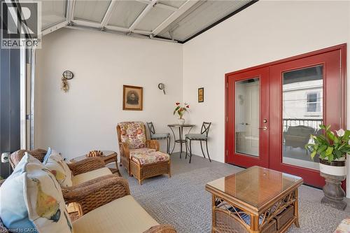 Carpeted outdoor living space featuring a roll-up glass panel door, white painted walls, and red double glass-paneled doors with brushed nickel hardware - 23 Market Street W, Port Dover, ON 