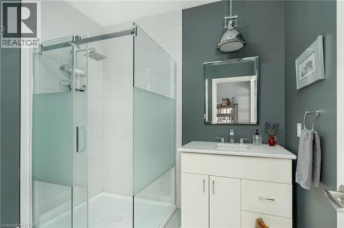 Frosted glass shower enclosure with a rain showerhead, white vanity with integrated sink, rectangular framed mirror, and a chrome pendant light fixture - 23 Market Street W, Port Dover, ON 