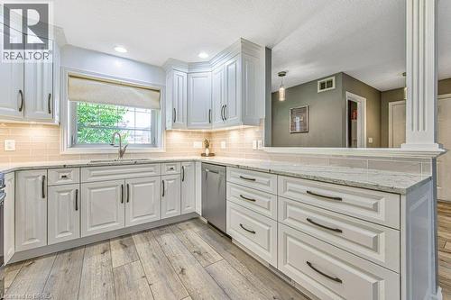 White cabinetry with dark hardware, undermount sink with a gooseneck faucet, light-toned tile backsplash, recessed lighting, and wood-finish flooring - 423 Poldon Drive, Norwich, ON 