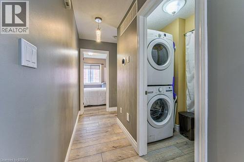 Hallway featuring wood-finish flooring, a pendant light fixture, and a laundry closet with stacked appliances - 423 Poldon Drive, Norwich, ON 
