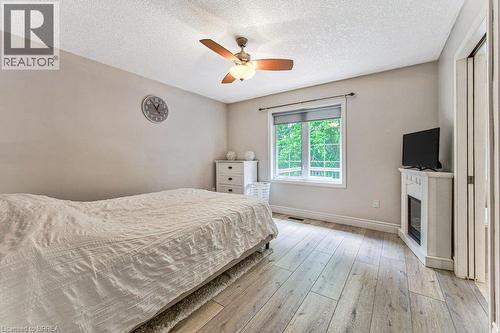 Wood-finish flooring, ceiling fan with integrated lighting, a window with a white frame, and a decorative fireplace - 423 Poldon Drive, Norwich, ON 