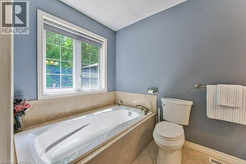 Bathtub with tile surround, window with roller shade, and tiled flooring - 423 Poldon Drive, Norwich, ON 