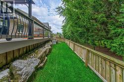Expansive green space featuring a wood fence, mature evergreen trees, and a rock garden bordering the deck - 