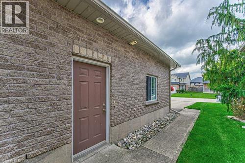 Brick exterior with a side entrance door, single window, concrete pathway, and landscaped gravel bed - 423 Poldon Drive, Norwich, ON 