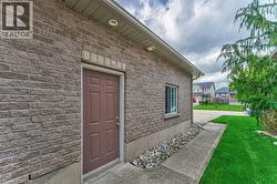 Brick exterior with a side entrance door, single window, concrete pathway, and landscaped gravel bed - 