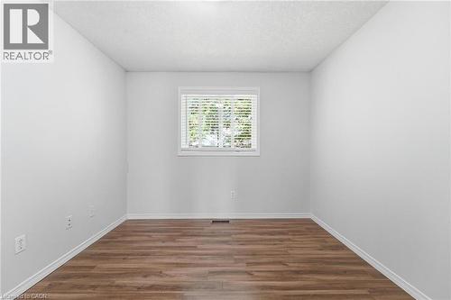 Wood-finish flooring with white baseboards, bright white walls, and a window with horizontal blinds - 449 Exmoor Street, Waterloo, ON 