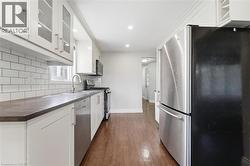 White cabinetry with glass-front uppers, stainless steel appliances, dark countertops, white subway tile backsplash, and wood-finish flooring - 