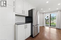 White cabinetry, subway tile backsplash, stainless steel refrigerator, dark countertops, and wood-finish flooring - 