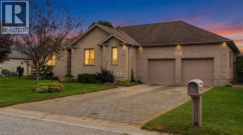Brick exterior featuring a two-car garage with individual doors, a paved driveway, and established landscaping - 515 Woodward Drive, Mount Brydges, ON 
