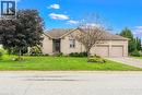 Beige brick exterior with a two-car garage, front lawn, and mature trees - 515 Woodward Drive, Mount Brydges, ON 