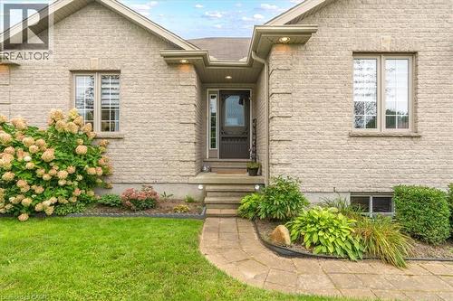 Stone-finish exterior with accent lighting, dark-paneled front door, paved walkway, and established landscaping - 515 Woodward Drive, Mount Brydges, ON 