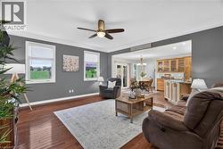 Wood-finish flooring, ceiling fan with integrated lighting, multiple windows, and a clear line of sight to the adjacent kitchen and dining area - 