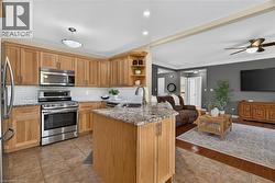 Open-concept kitchen with wood-finish cabinetry, stainless steel appliances, granite countertops, and tile flooring - 